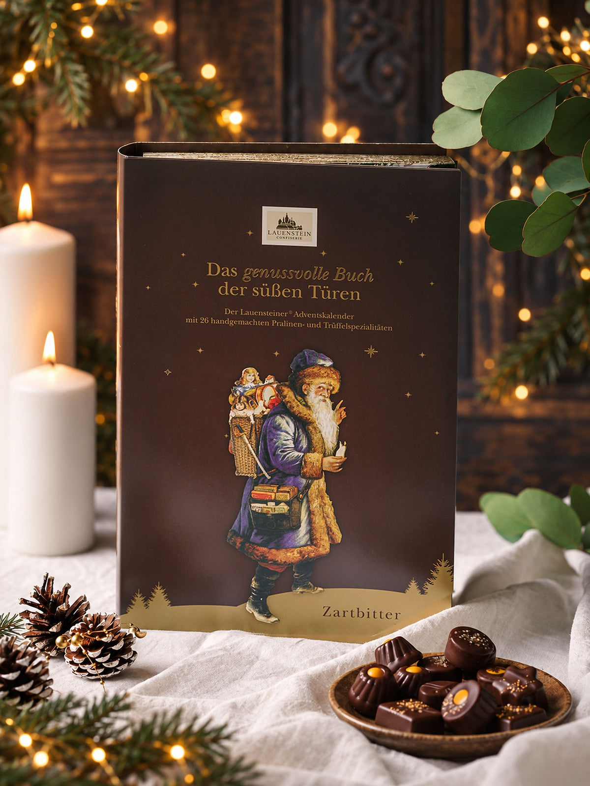 Lauensteiner Adventskalender Buch Zartbitter 340g von Confiserie Lauenstein mit braunem Einband und Weihnachtsmann, dekoriert mit Kerzen, Tannenzweigen und Zartbitterpralinen
