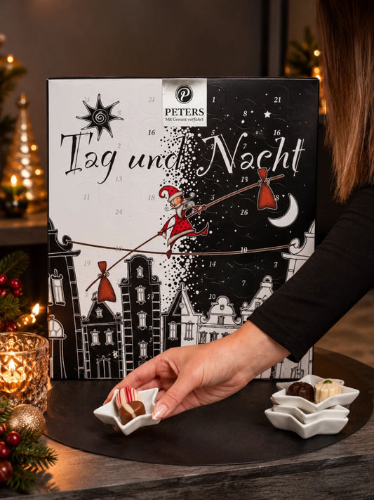 Tag & Nacht Adventskalender 275g von PETERS Pralinen in weihnachtlicher Dekoration mit Kerzen, Tannenzweigen und angerichteten Schokoladenpralinen